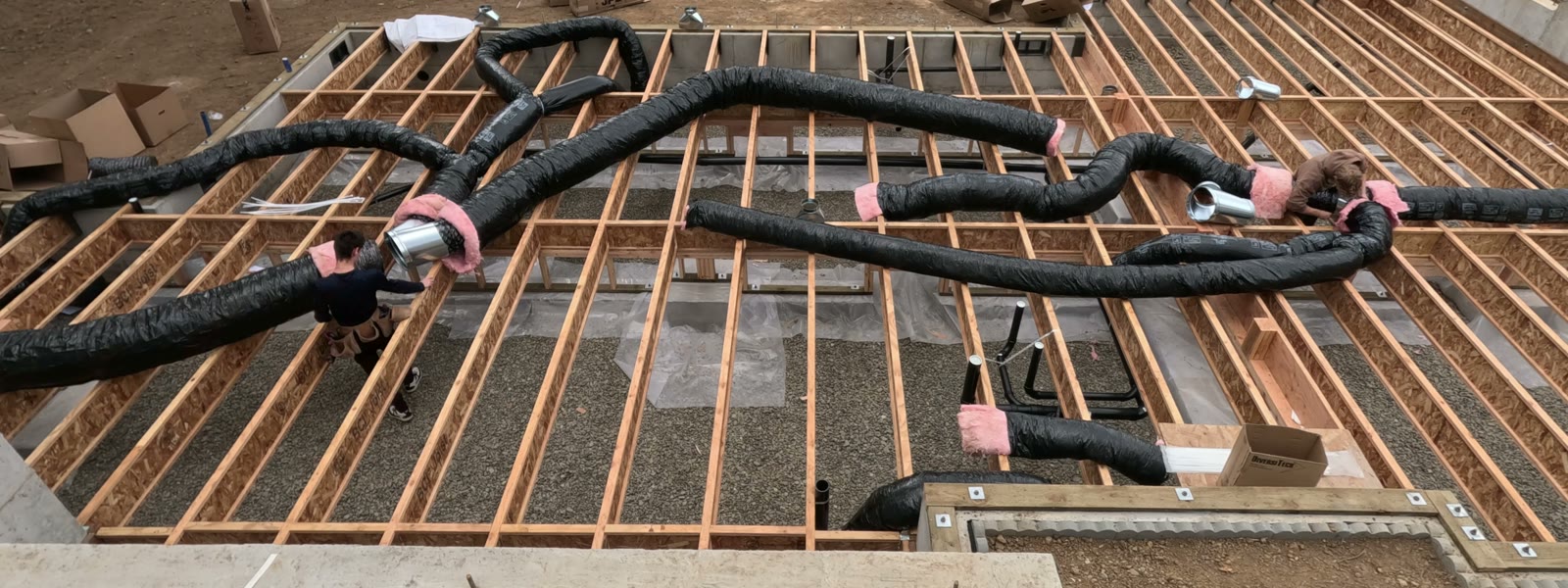 Pacific Peak crew running insulated flex duct across floor joists on a new home