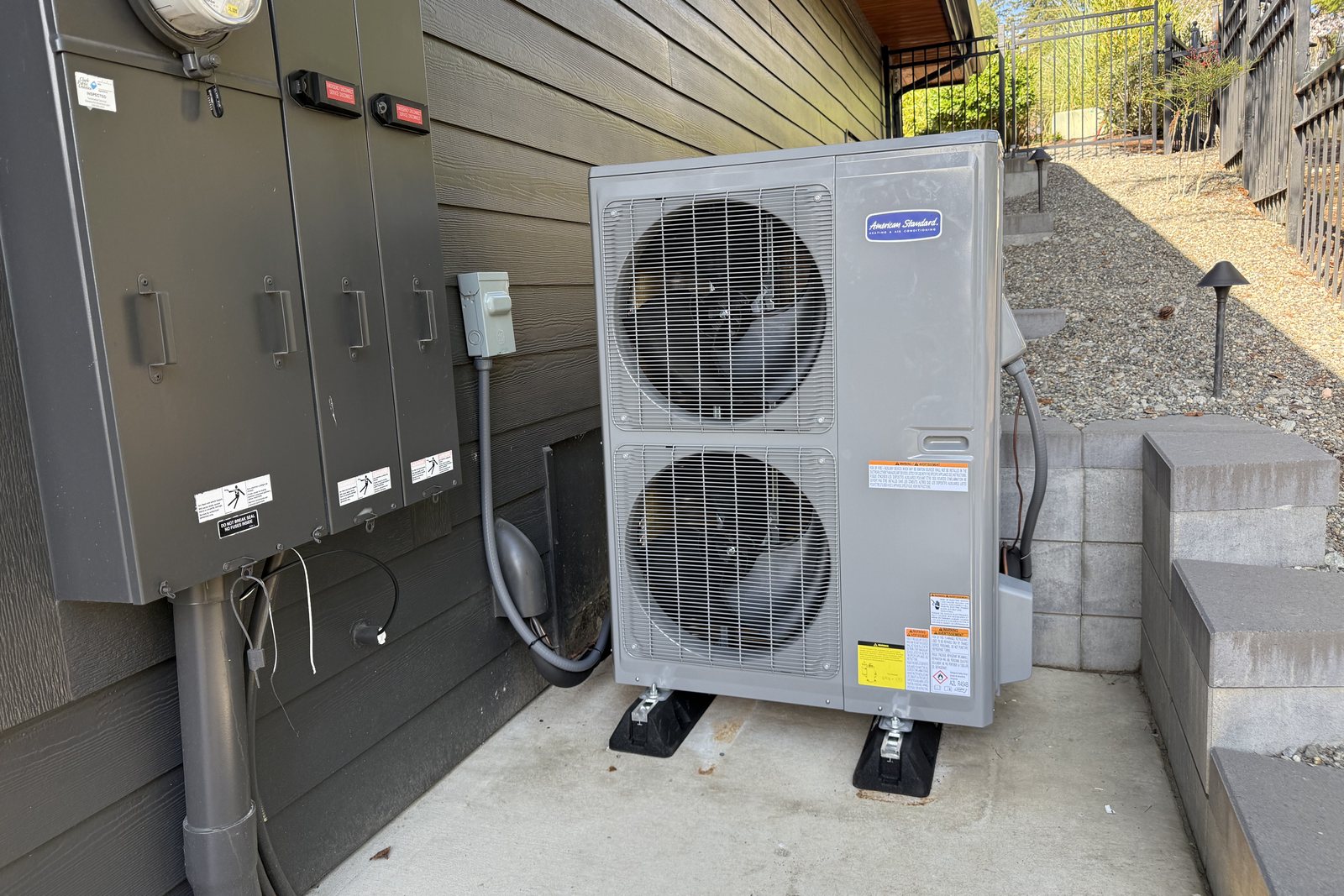 American Standard outdoor unit on rubber isolation pads beside a home's electrical panel