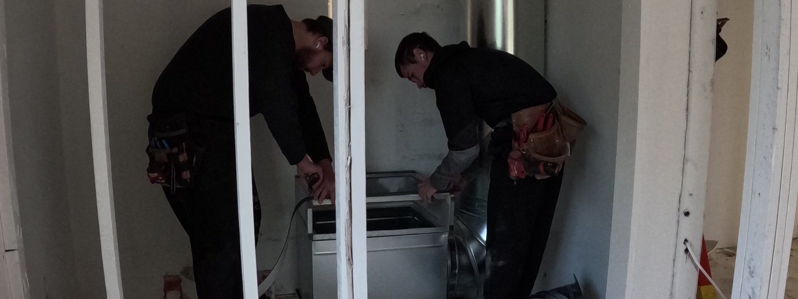 Two Pacific Peak Mechanical installers setting a plenum in a new-construction mechanical closet