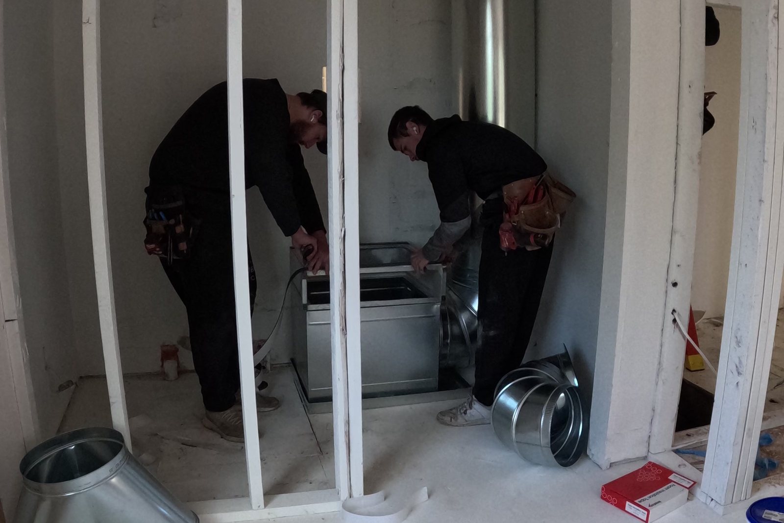 Two Pacific Peak Mechanical installers fitting a plenum in a mechanical closet