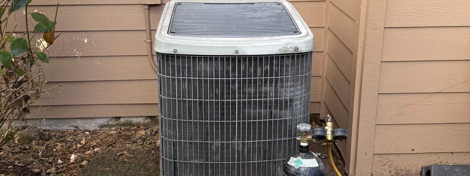 Old outdoor AC unit with service gauges connected, ready for a changeout