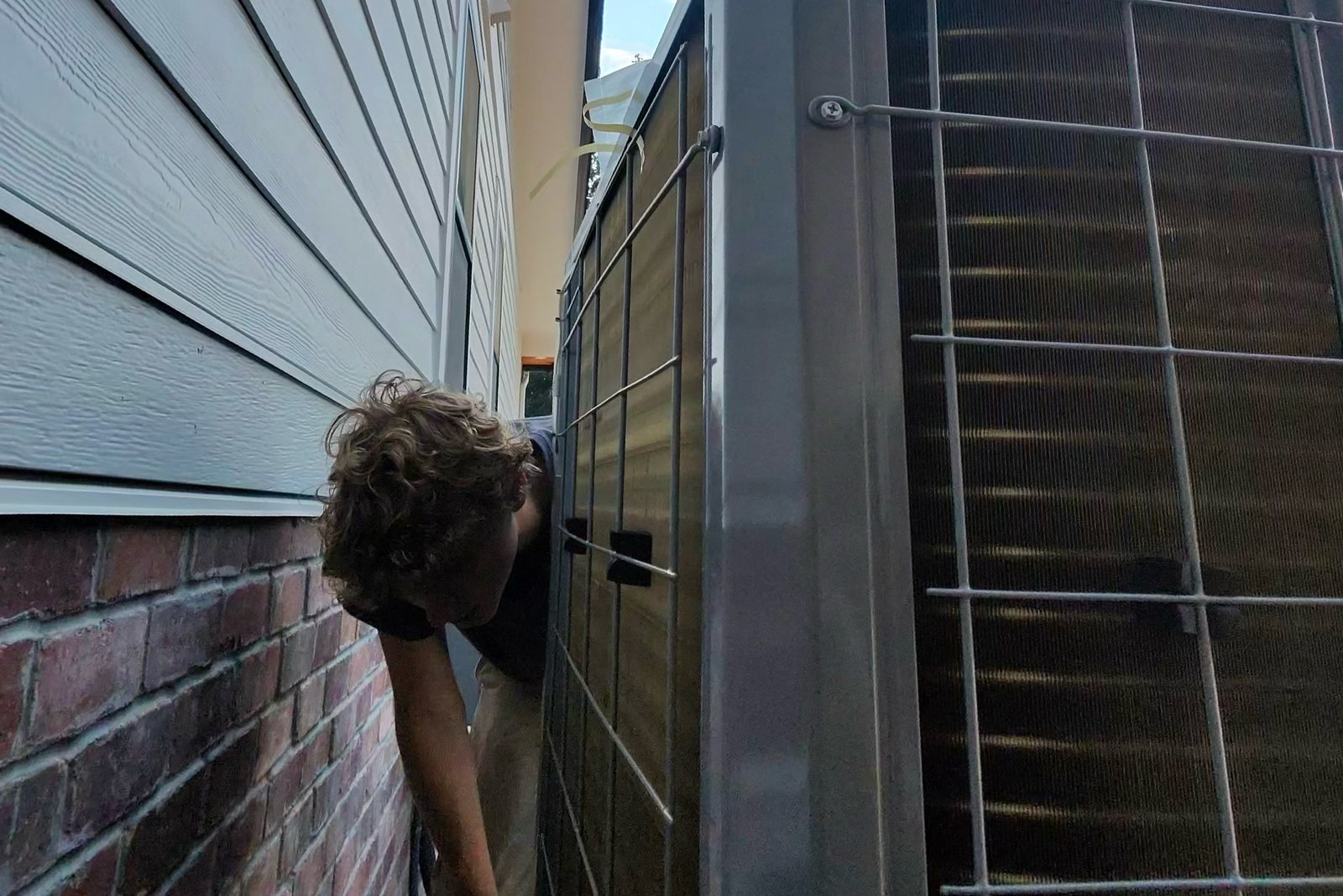 Pacific Peak Mechanical technician checking an outdoor condenser in a narrow side yard