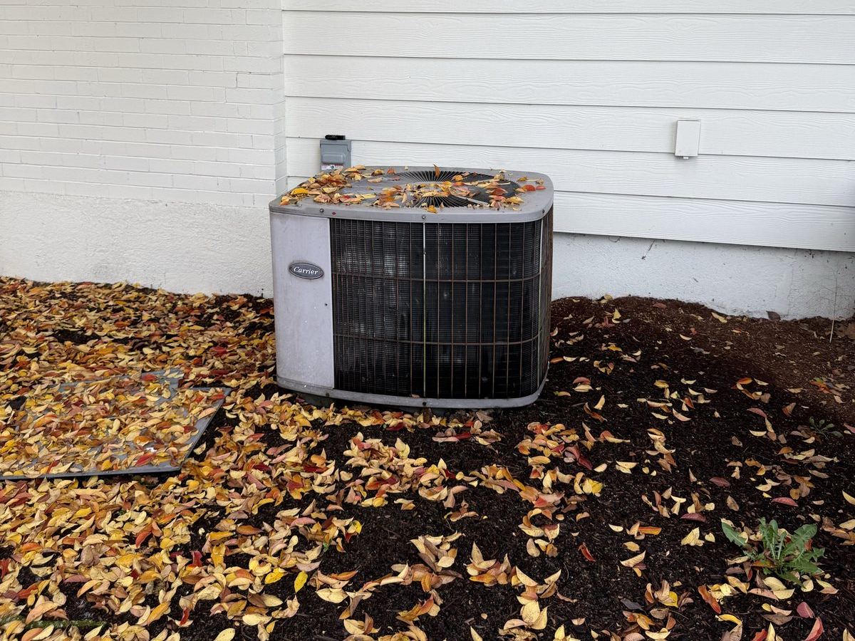 An aging outdoor HVAC unit beside a house, covered in fallen leaves