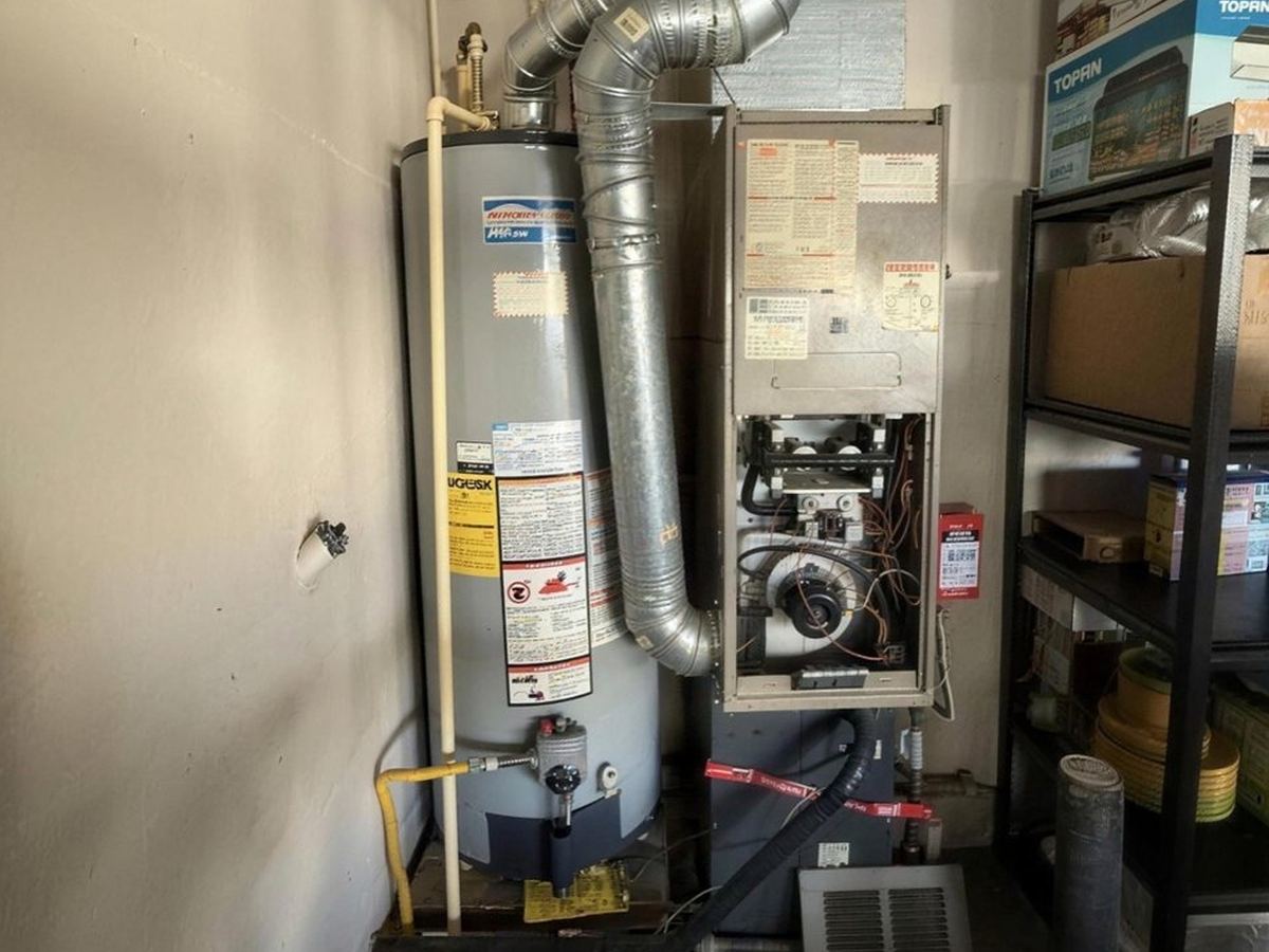 An older gas furnace beside the water heater in a closet, front panel off during a diagnosis